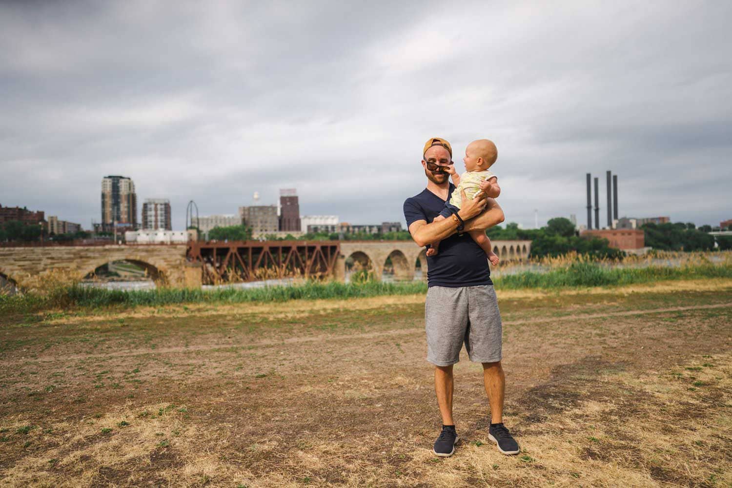 Adirondack Photography A Dad Holding A Baby In Front Of A Bridge For A Photoshoot