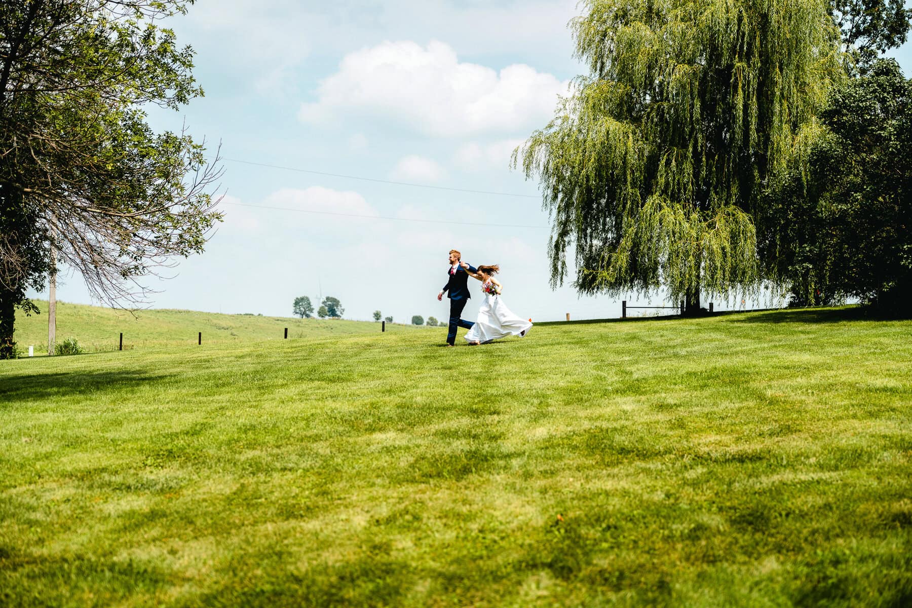 A Bride And Groom Running Across A Farm Field