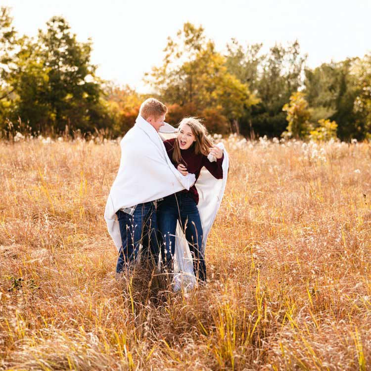 Couple Wrapped In Blanket In Field Posing For Engagement Photo