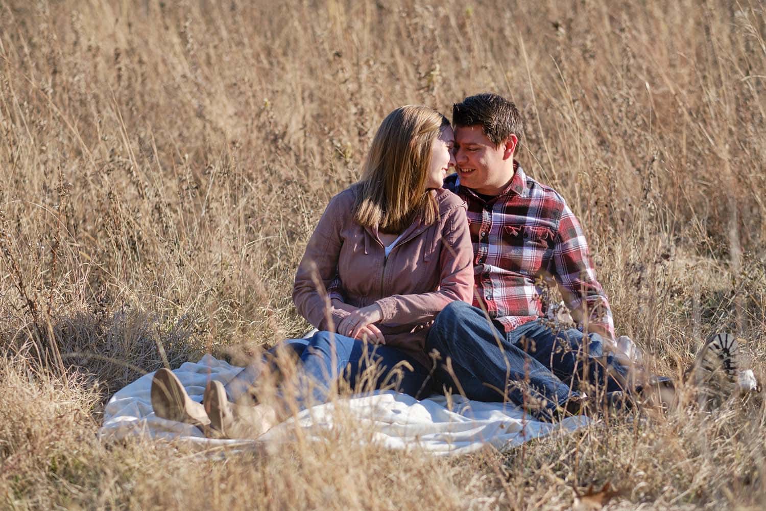 Adirondack Photography A Couple Sitting On A Blanket In Tall Grass.